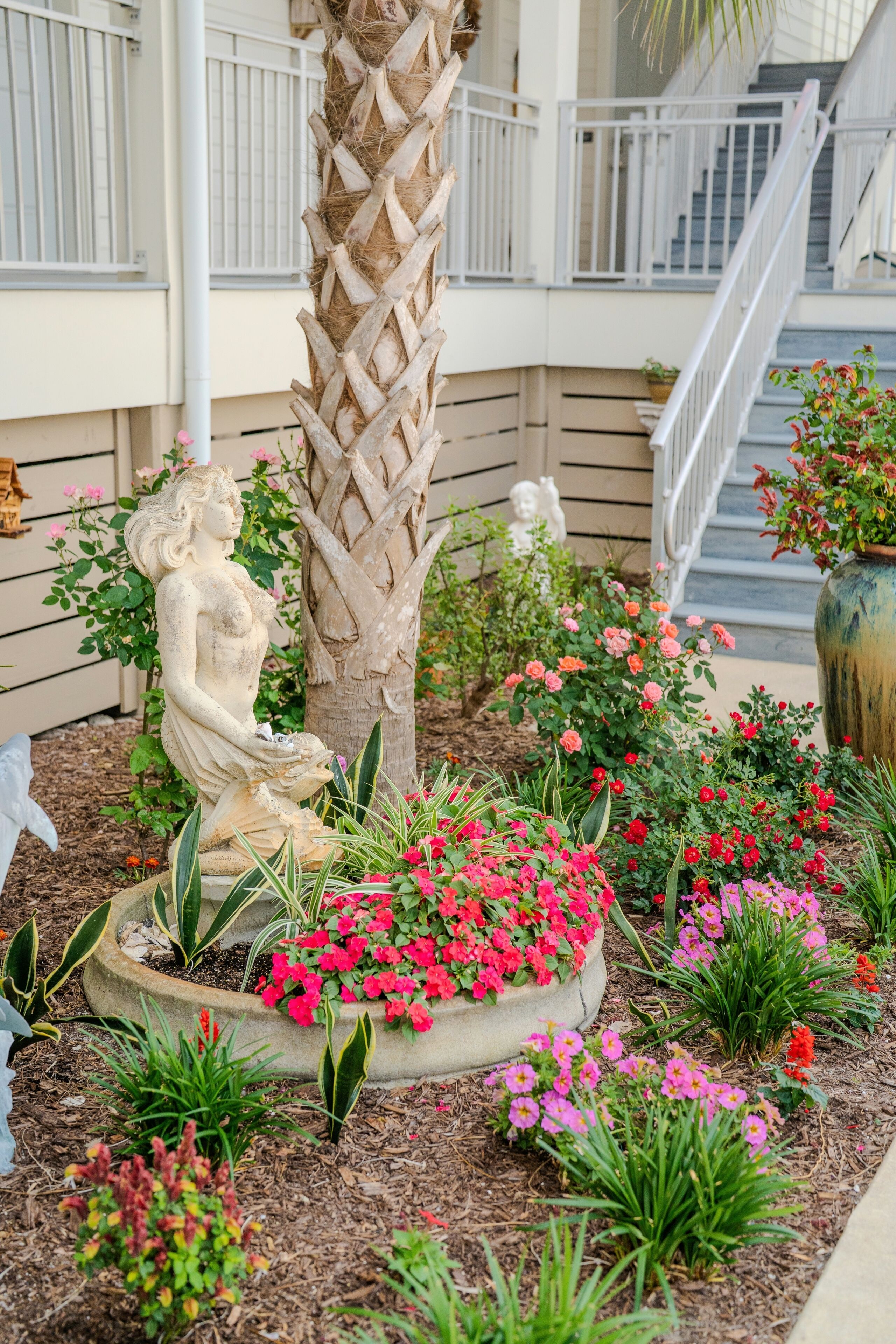 A garden with a statue, a palm tree, and various flowers.