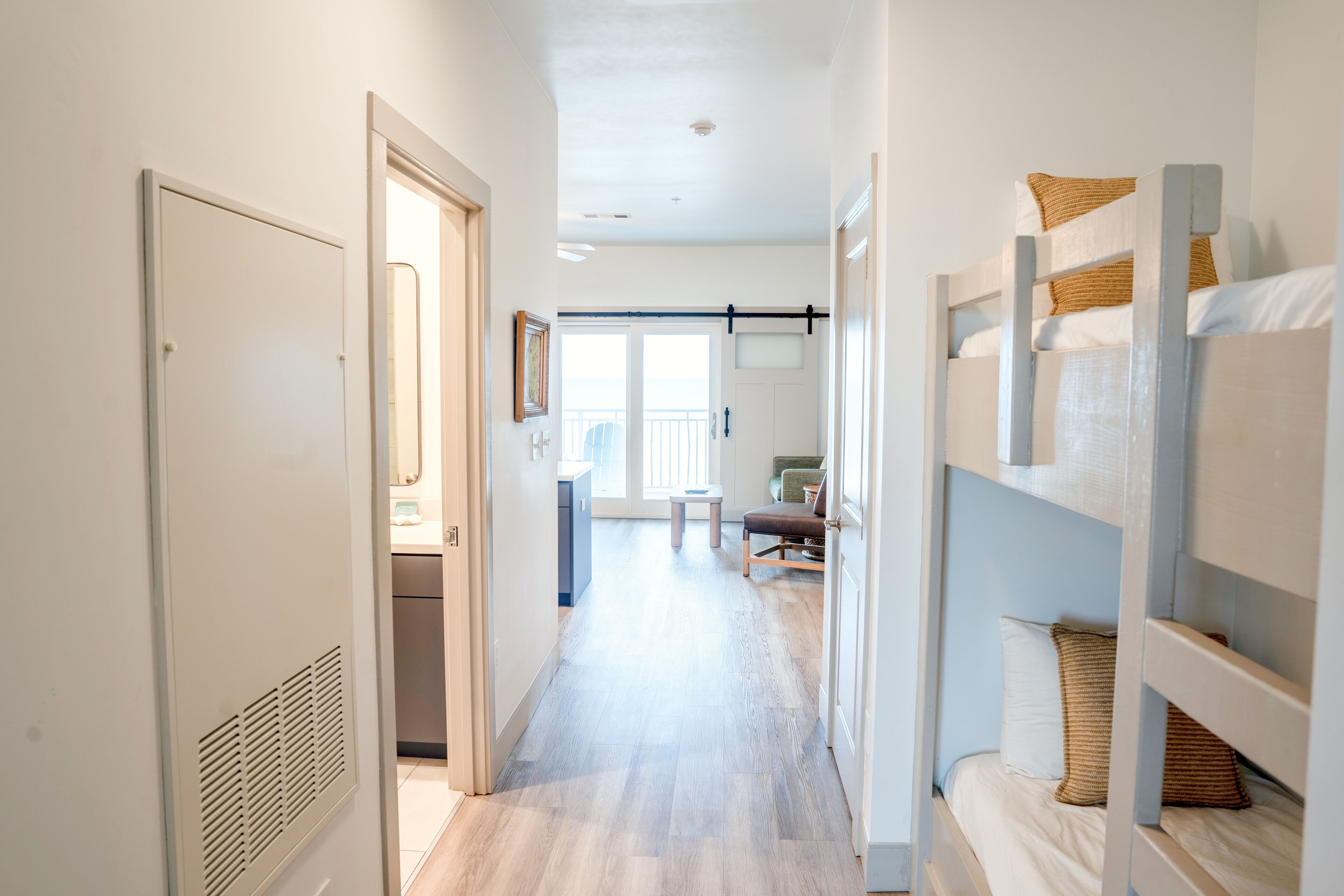 A corridor leading to a bedroom with bunk beds, a door, and a view of a balcony.