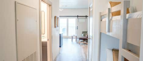 Un passadís que condueix a una habitació amb literes, una porta i vista a un balcó.