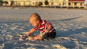 Un enfant joue dans le sable, avec un hôtel en arrière-plan.