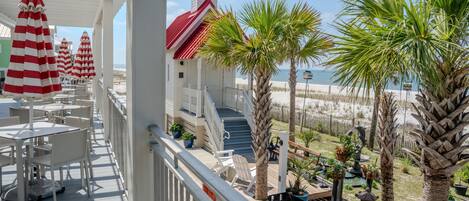 A covered outdoor area with white chairs and red-striped umbrellas, a small white building with a red roof, and palm trees.