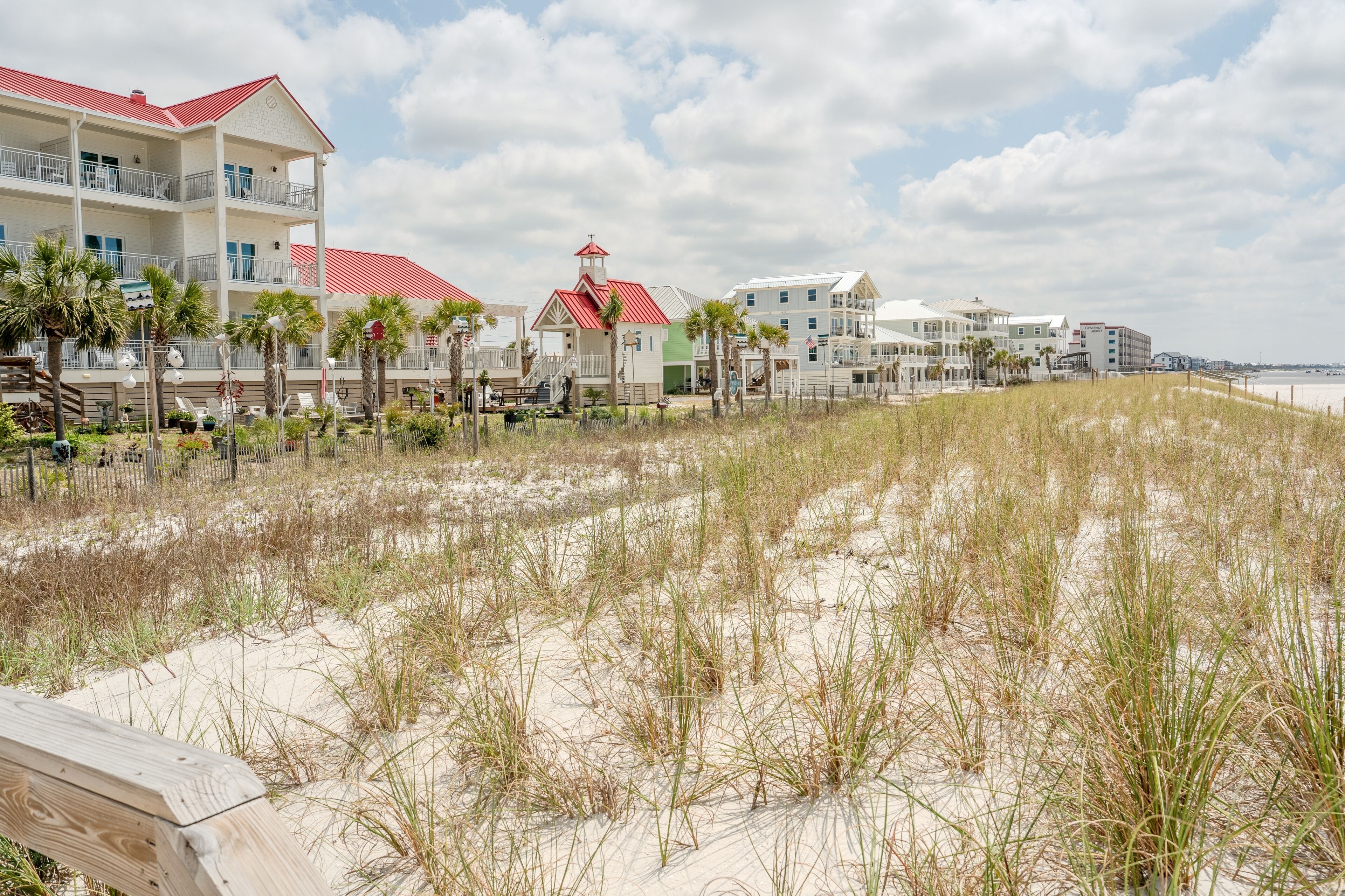 A beachfront hotel with multiple floors, a red-roofed building, and a beach in the foreground.