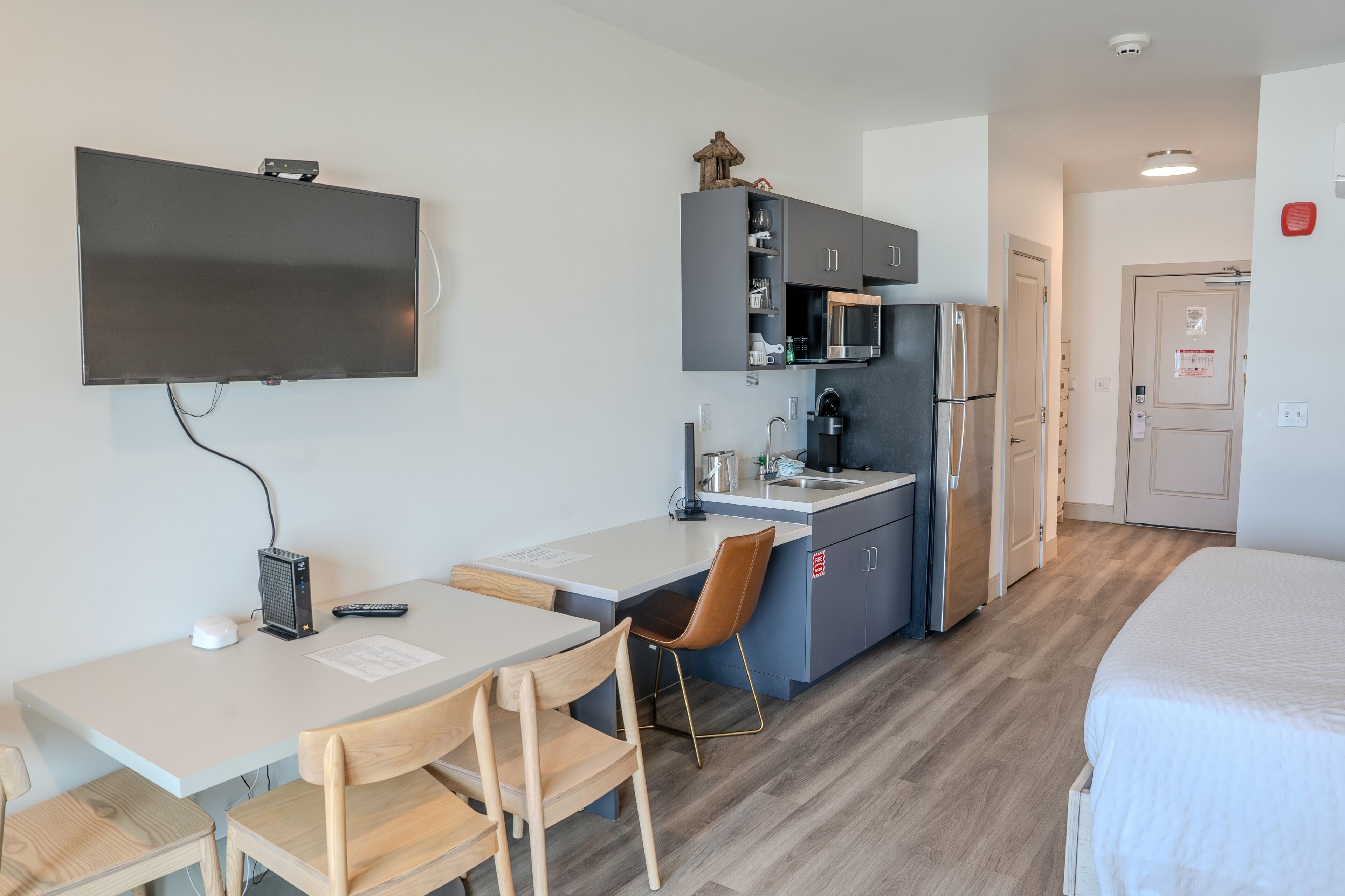 A compact hotel room with a kitchenette, a flat-screen TV, a desk with a chair, and a bed.