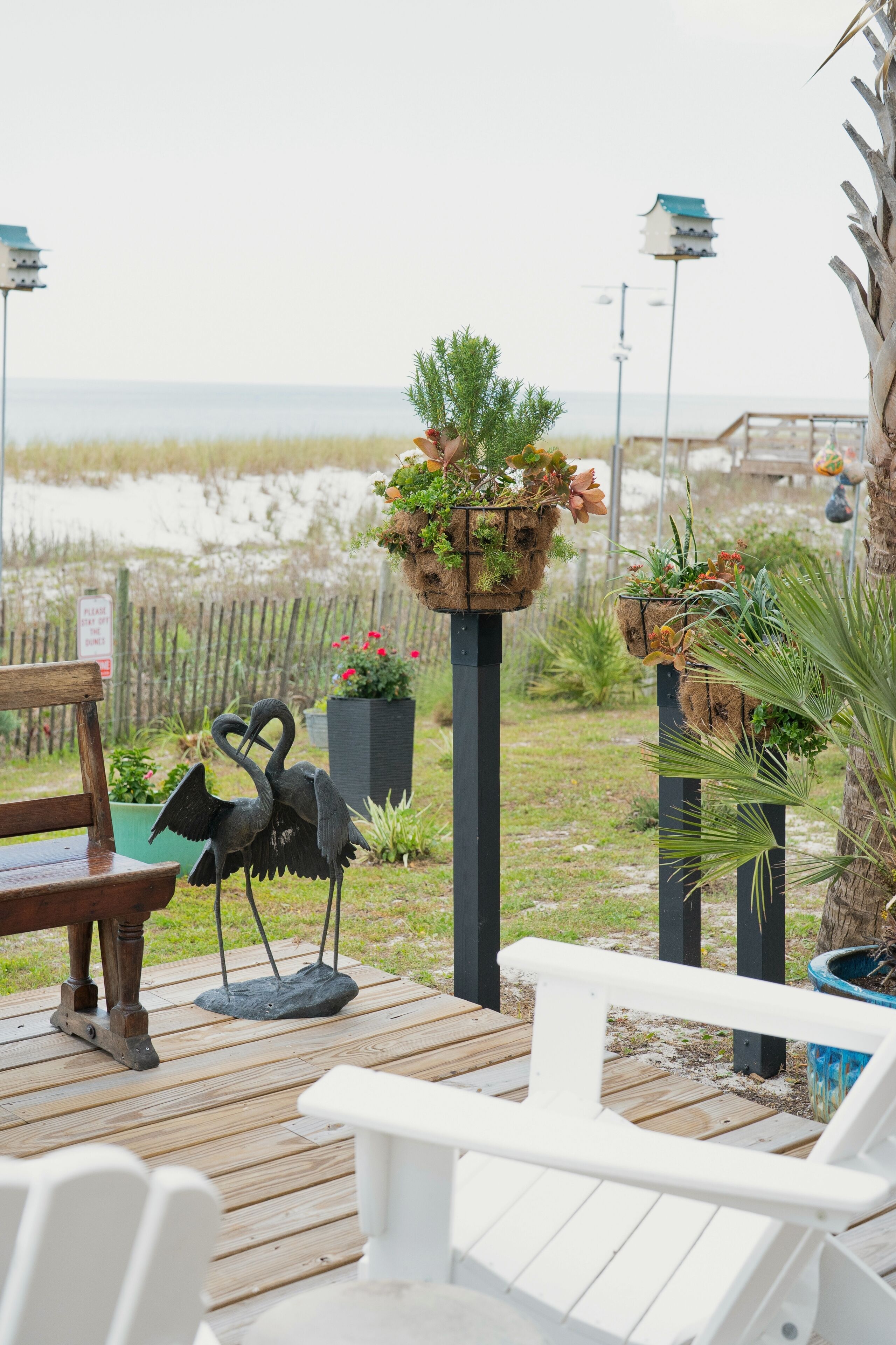 A wooden deck with outdoor seating, a bird sculpture, and hanging planters with greenery.