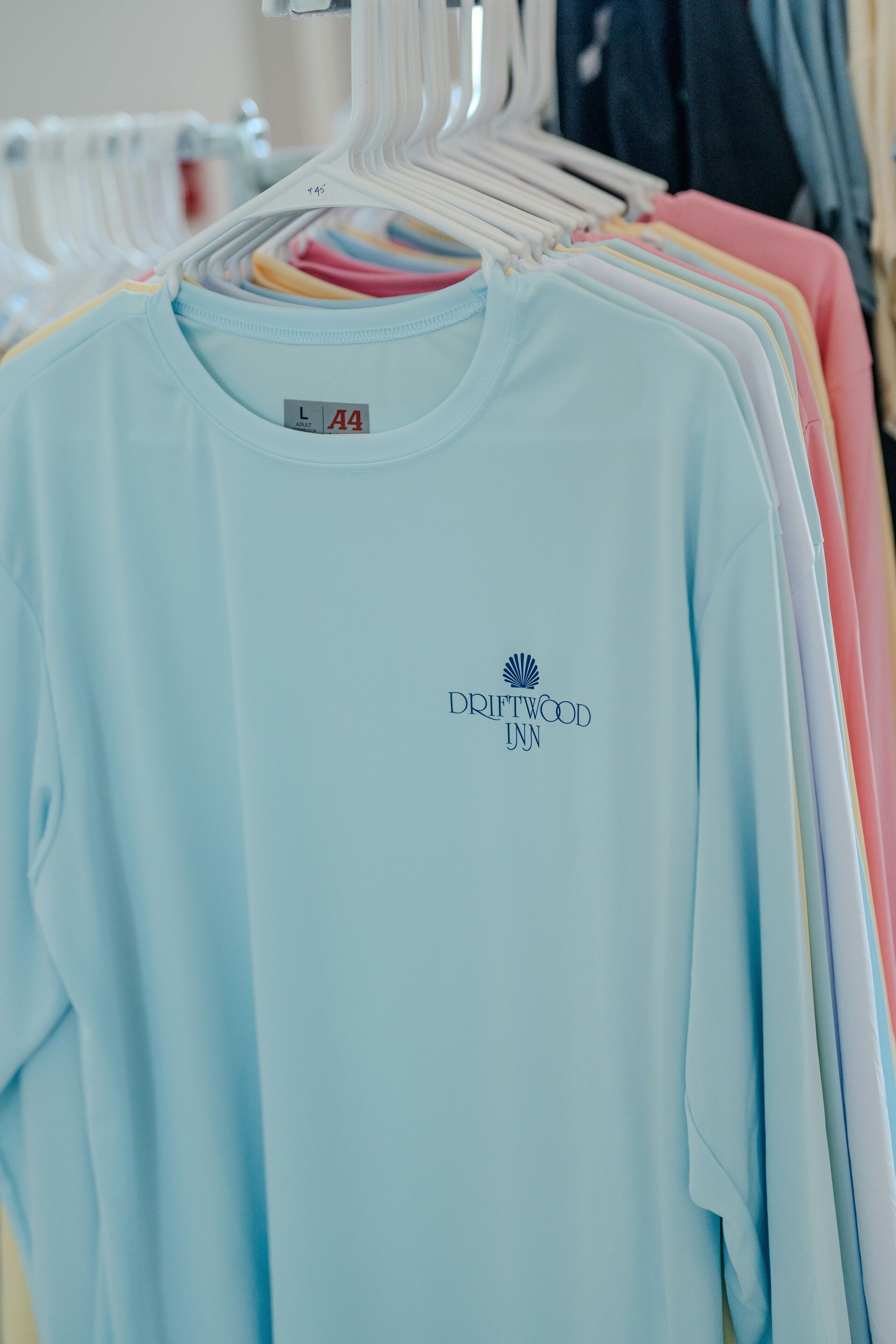 En lyseblå t-shirt med Driftwood Inn logo på en bøjle.
