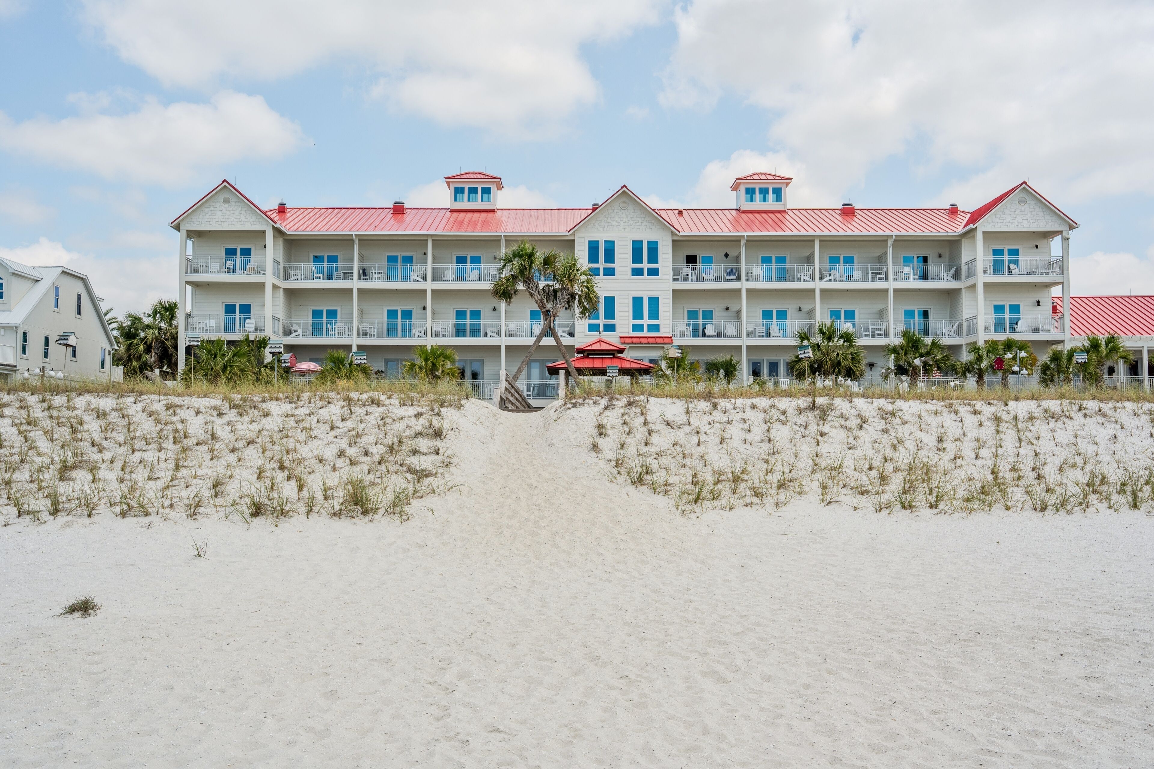 Ein Strandhotel mit rotem Dach, mehreren Balkonen und einem Sandstrand davor.