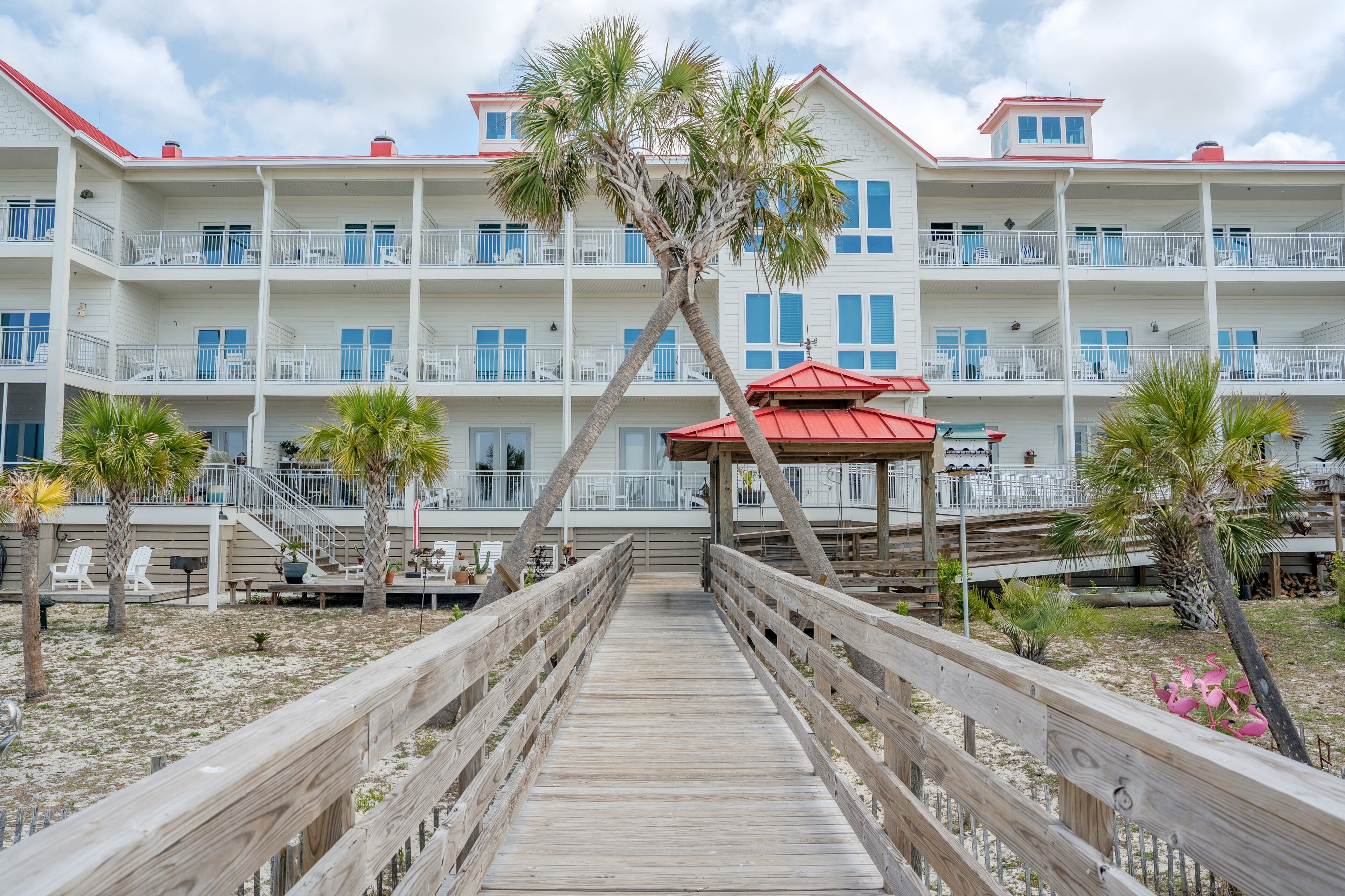 A beachfront hotel with multiple balconies, a wooden walkway, and palm trees.