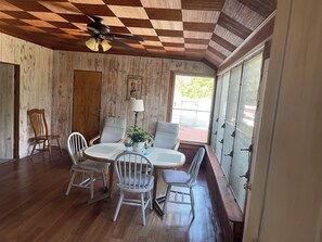 A dining area with a wooden ceiling, a ceiling fan, a table with chairs, a potted plant, and a window with a view of the outside. - Charming Southold Retreat with In Ground Pool – Walk to Founder’s Beach (Southold)