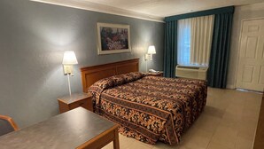 Une chambre d’hôtel avec un lit, un bureau, deux lampes de chevet, un tableau au mur et une fenêtre avec des rideaux.