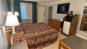 Une chambre d’hôtel équipée d’un lit, d’un bureau, d’une commode, d’une télévision et d’une kitchenette.