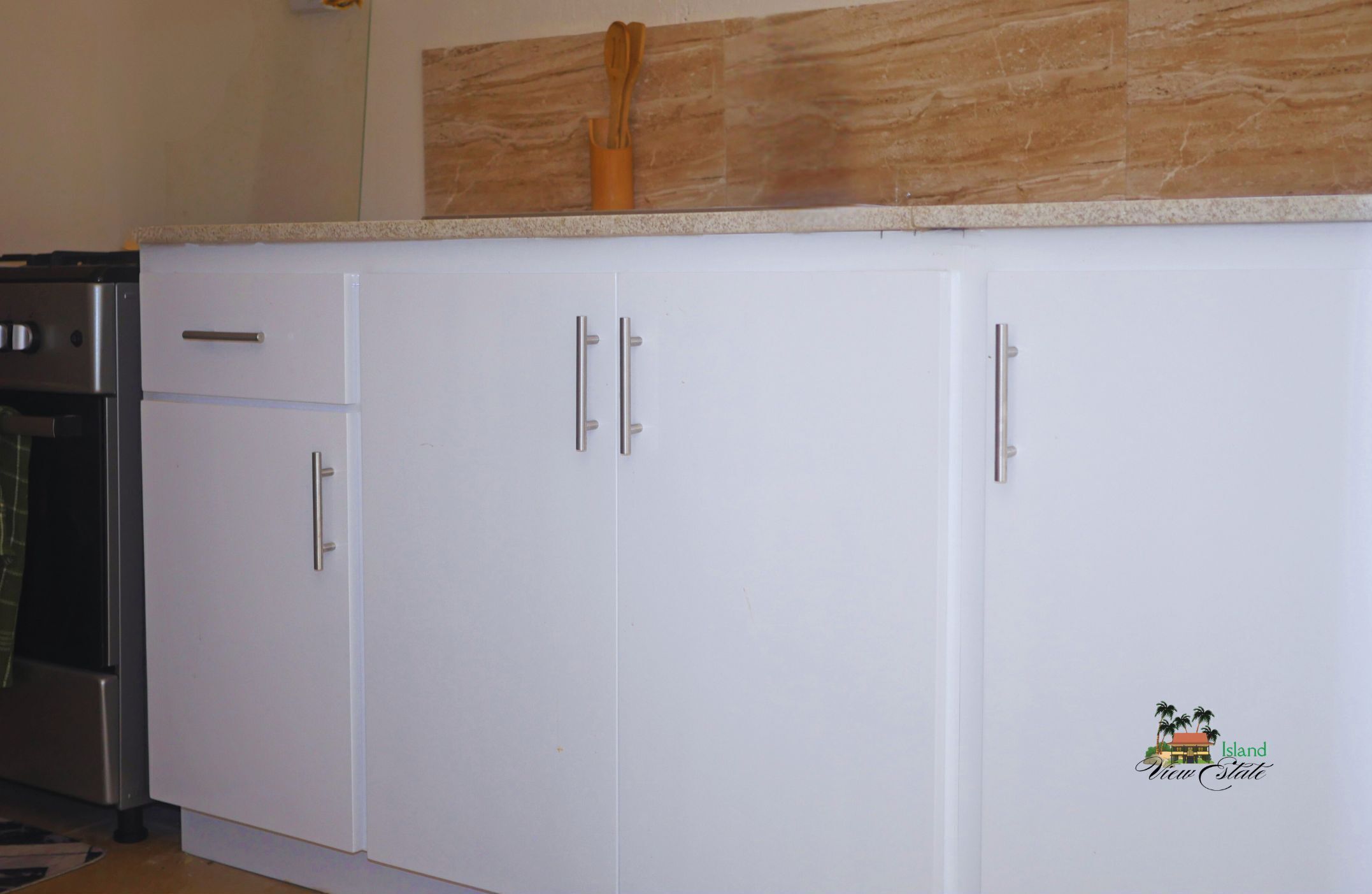 A kitchen with white cabinets, a wooden countertop, and a logo on the wall.