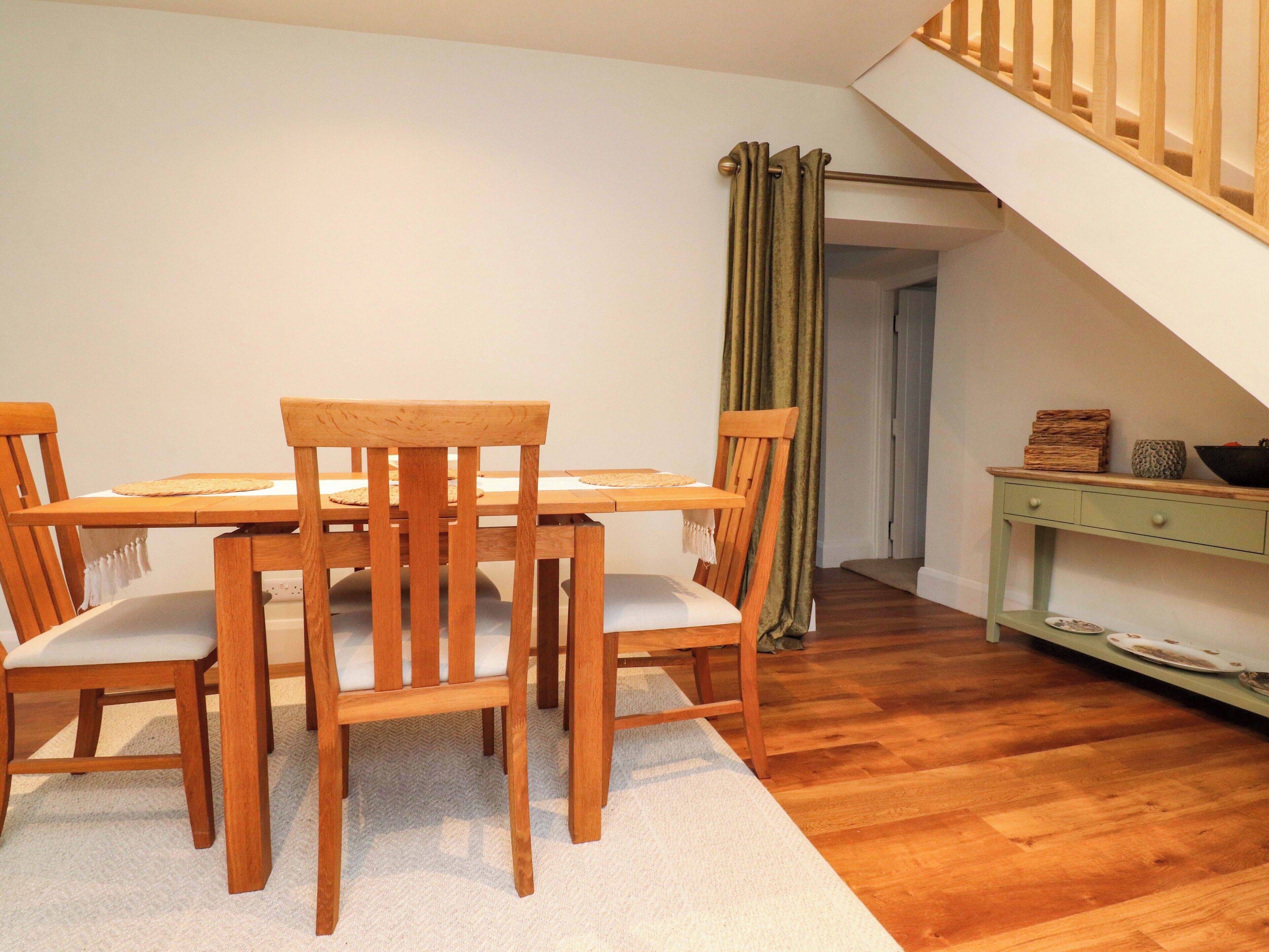 A dining area with a wooden table and chairs, a green curtain, and a staircase in the background.