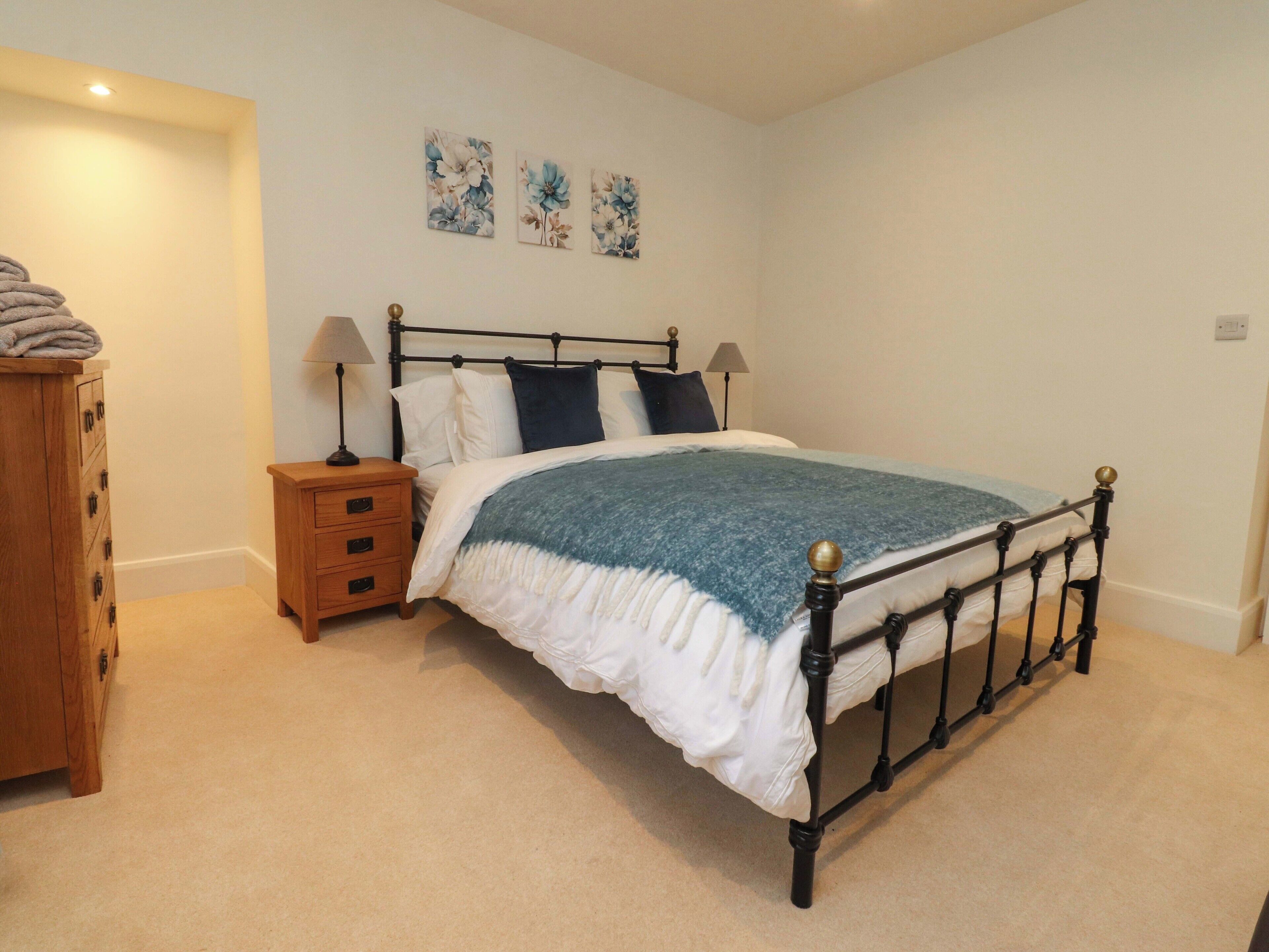 A bedroom with a bed, two nightstands, a wooden dresser, and three floral wall art pieces.