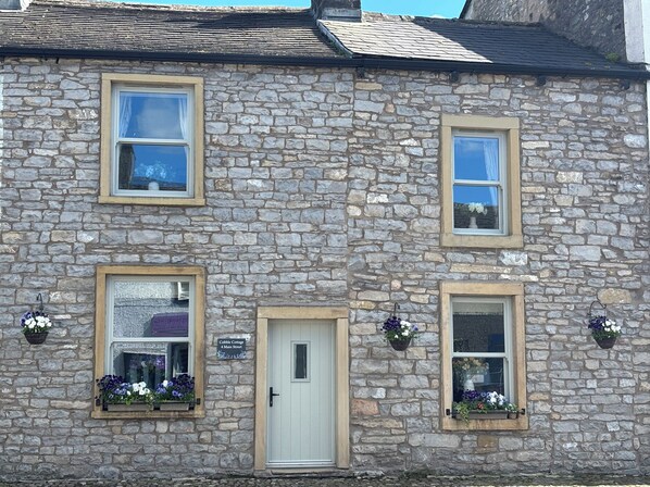 A stone building with a white door, two windows with flower boxes, and a sign indicating 'Cobble Cottage 4 Main Street.' - Cobble Cottage (Clitheroe)