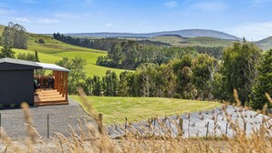 Un bâtiment moderne doté d’une terrasse en bois et offrant une vue sur des collines verdoyantes et une montagne lointaine.