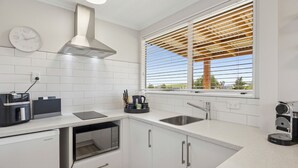 Une cuisine moderne avec des meubles blancs, un évier en acier inoxydable et une fenêtre équipée de stores horizontaux.
