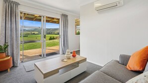 Un salon moderne doté d’une grande porte-fenêtre coulissante donnant sur un balcon, d’un canapé blanc, d’une table basse en bois et d’un climatiseur fixé au mur.