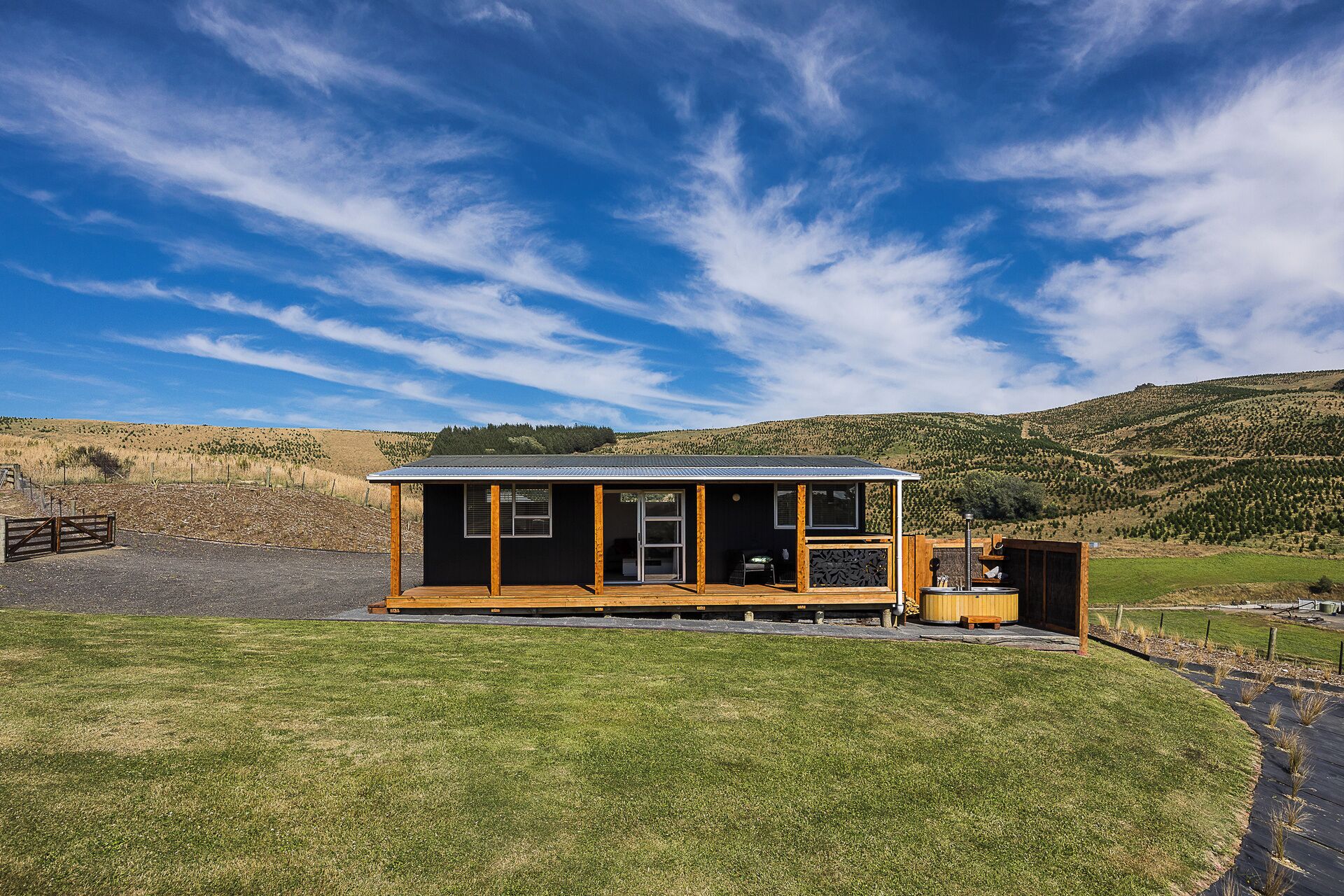 A small, single-story cabin with a metal roof, a wooden deck, and a large window.