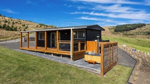 Une cabane moderne dotée d’une grande terrasse, d’un bain à remous et offrant une vue panoramique sur les collines environnantes.