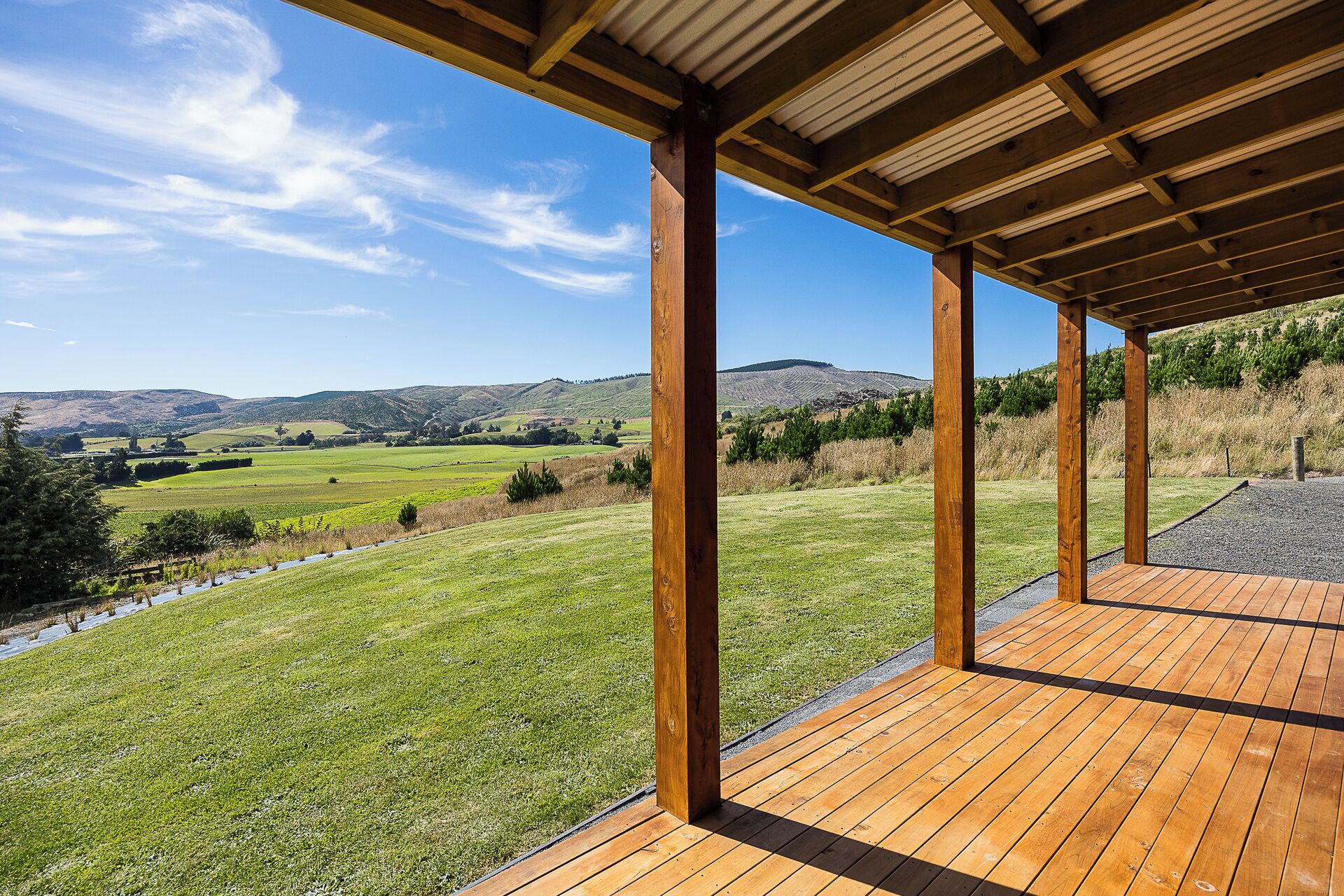 A wooden deck with a view of a green field and distant hills.