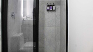 Eine Duschkabine mit Glas, eine Marmorwand, eine kleine Ablage mit Flaschen und ein sichtbares WC.
