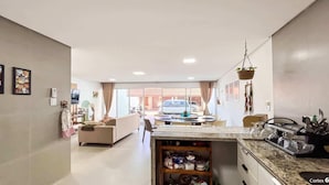 A modern living room with a sofa, dining table, and kitchen area with granite countertops. - Triplex em Porto de Galinhas a 50m da Praia Maracaipe (Ipojuca)