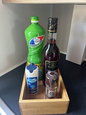 Eine Holzkiste mit einer grünen Flasche, einer dunklen Flasche, einem weißen Behälter und einem Einmachglas.