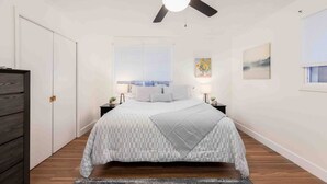 A bedroom with a bed, a ceiling fan, a window with blinds, a nightstand, and a wall-mounted painting. - Millcreek Basecamp - Pet friendly and Convenient! (Salt Lake City)