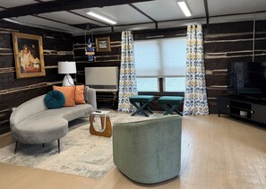 Una sala de estar con sofá, mesa de centro, televisor y ventana con cortinas.