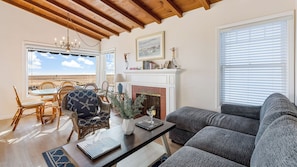 A living room with a fireplace, a dining area with wicker chairs, and a view of the beach. - Oceanfront Atelier by Avantstay Beachfront Balboa Peninsula Escape (Newport Beach)