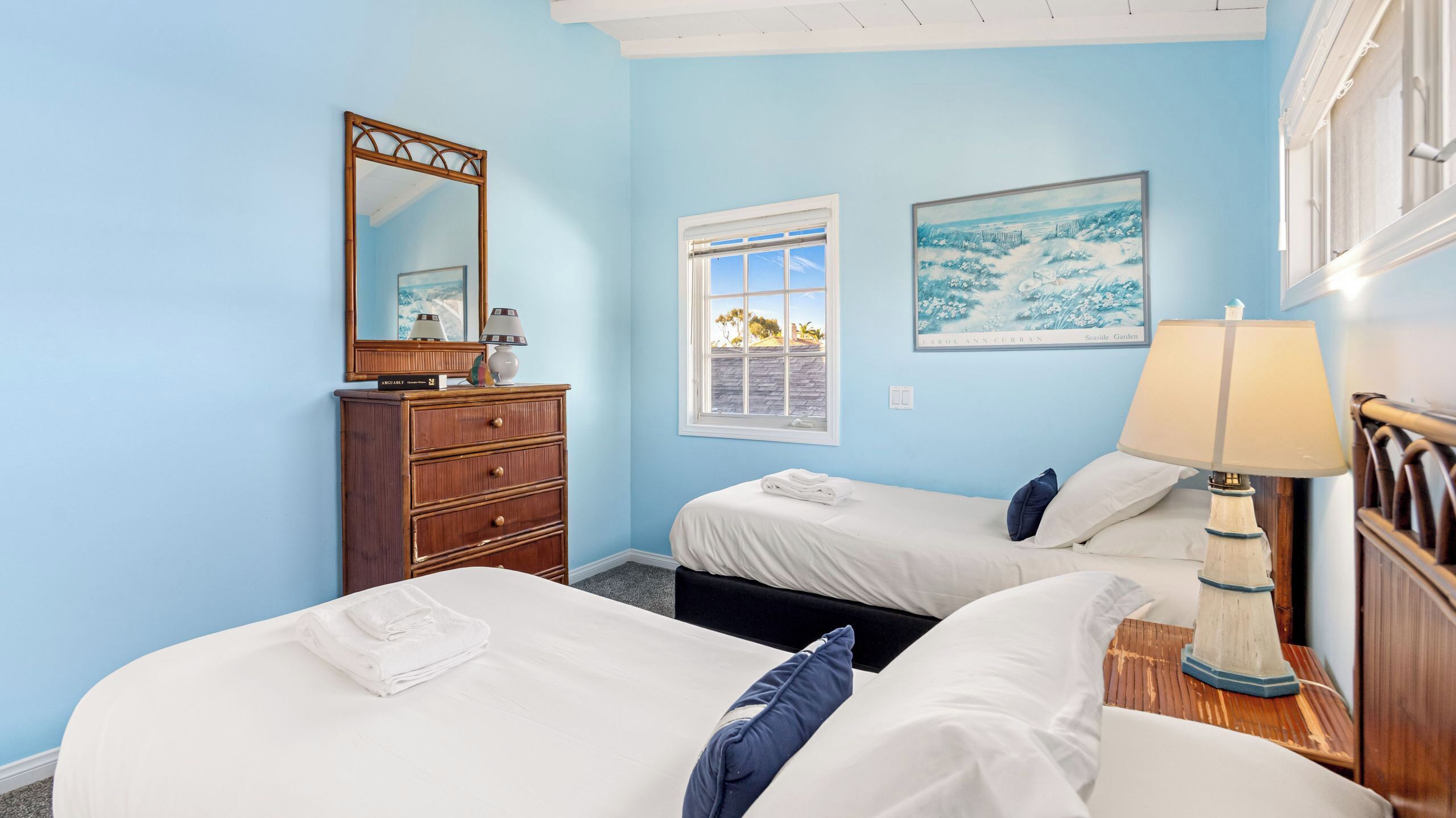 A room with two beds, a dresser, a lamp, and a painting.