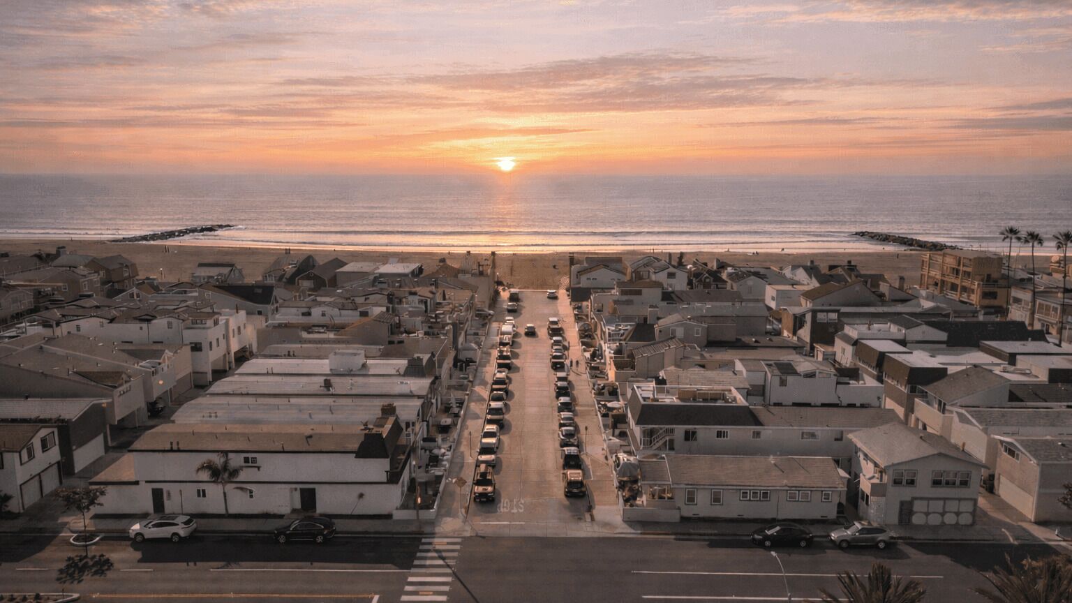 Une ville côtière avec une rue qui mène à la plage, des maisons et des voitures garées.