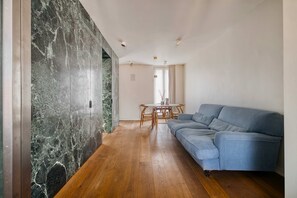 A spacious living room with a blue sofa, wooden flooring, a marble wall, and a dining area with a table and chairs. - w* | Stunning Apt w/ Private Terrace & Views (Milano)