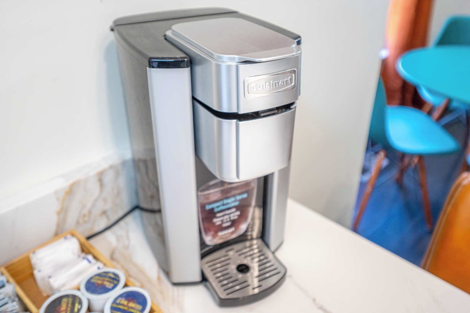 A Cuisinart espresso machine on a countertop with a marble backsplash and a blue chair in the background.