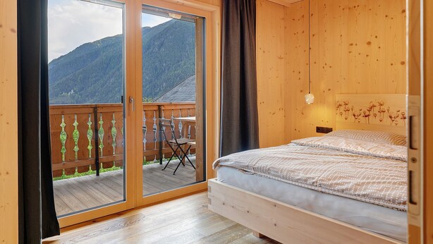 Una habitación de madera con una cama, una puerta corrediza de vidrio a un balcón y vistas a la montaña.