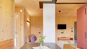 Un interior de madera con una mesa de comedor, sillas, un florero con flores, un televisor y un armario rojo.