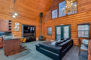 Interior de una cabaña de troncos con chimenea, televisor, sofá y comedor.
