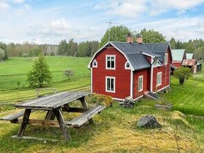 A red house with a sloped roof, a wooden picnic table, and a grassy field in the background. - 8 Person Holiday Home in Hogsby (Högsby)