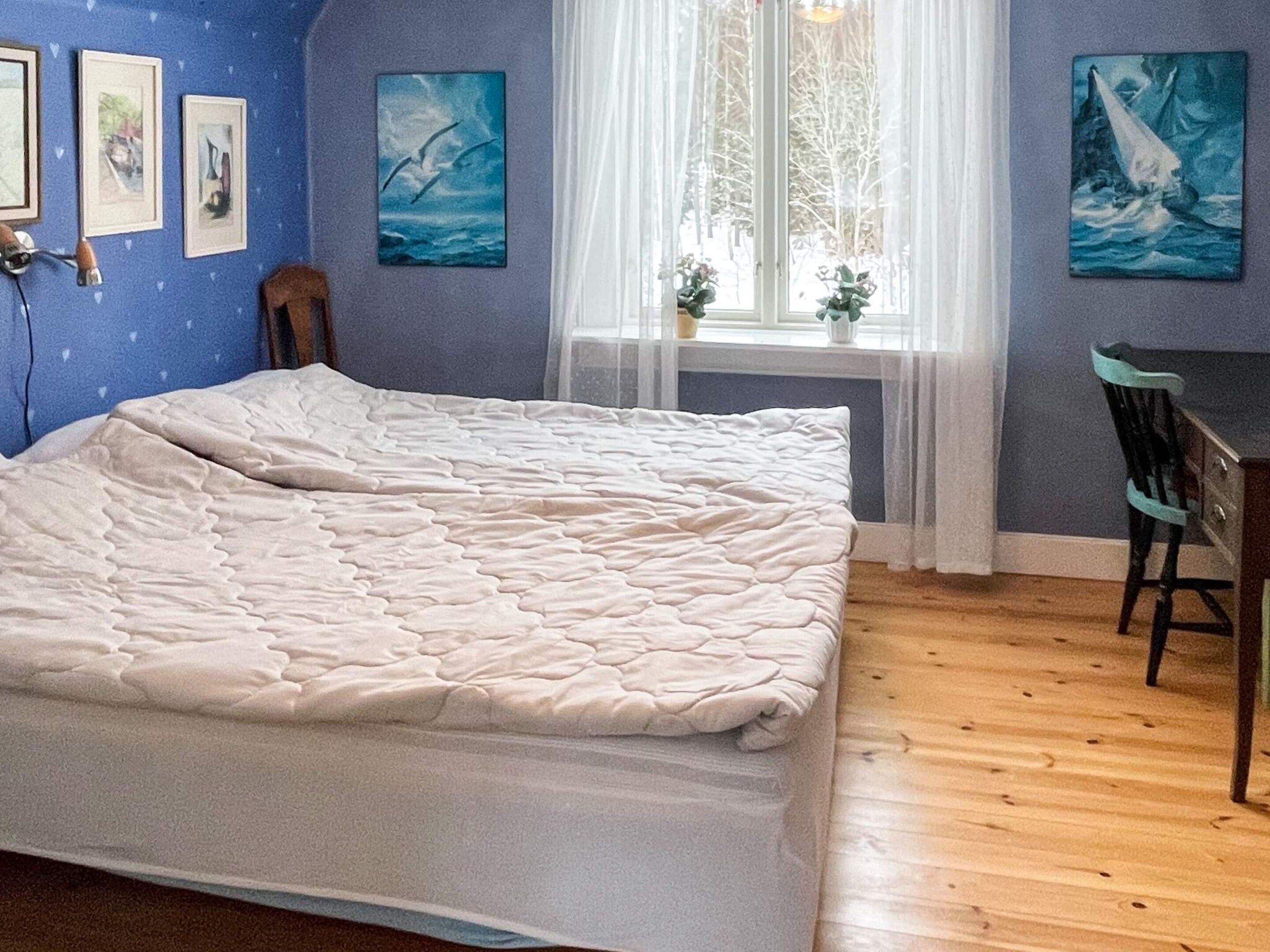 A bedroom with a bed, a chair, a window with curtains, and wall art.