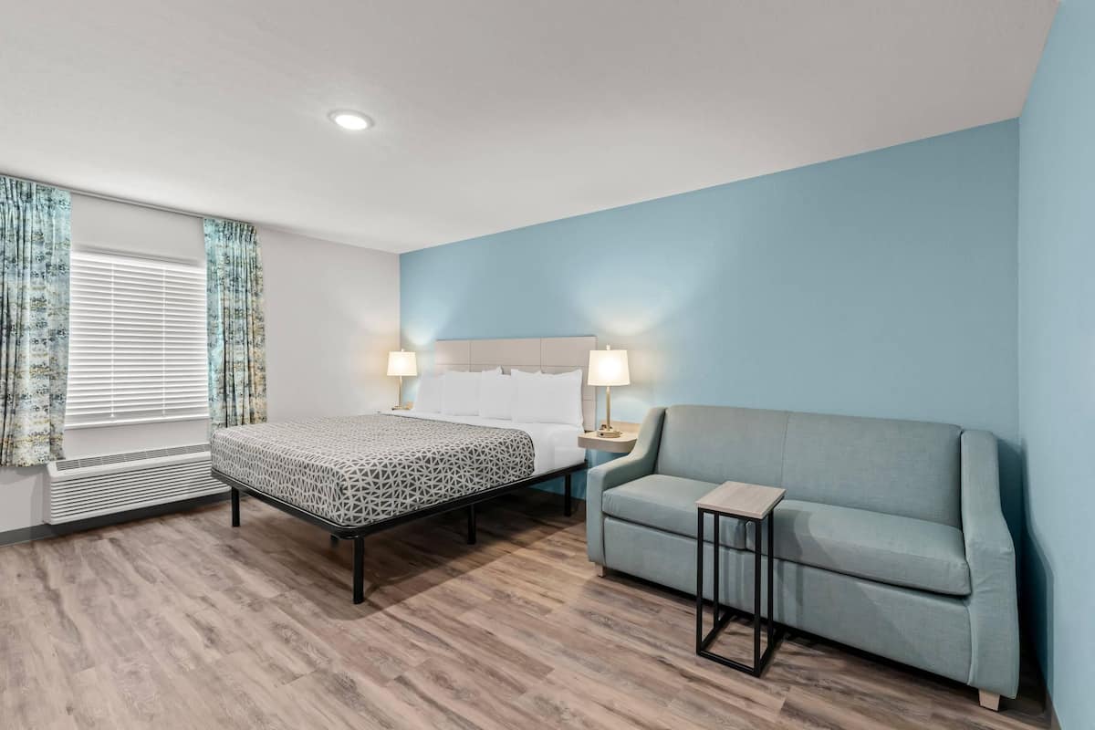 Una habitación de hotel con cama, sofá, mesita de noche y ventana con cortinas.