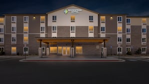 Um hotel com vários andares, teto plano, entrada coberta e uma placa com o nome 'Woodspring Suites'.