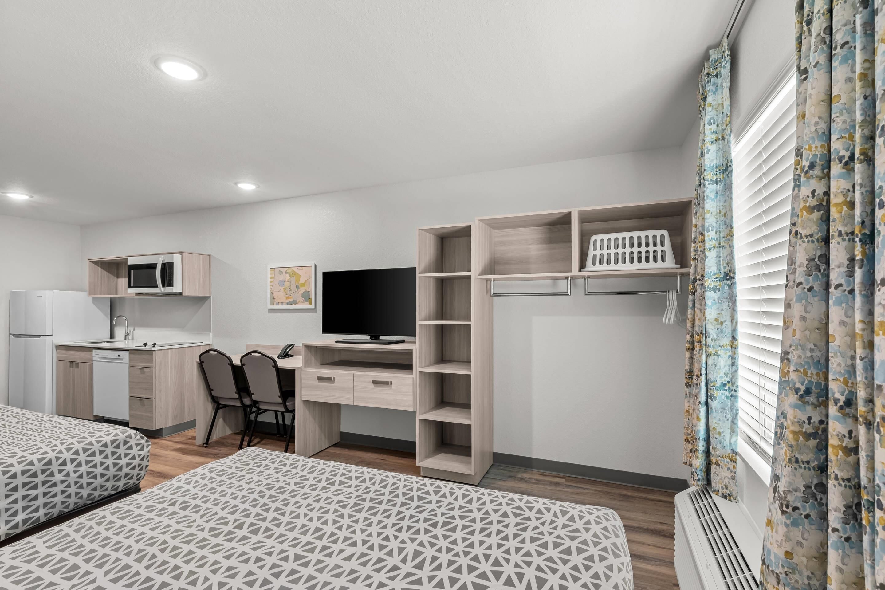 Une chambre dotée d’une kitchenette, d’une télévision, d’un bureau, de deux lits et d’une armoire.