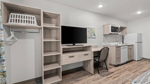 Quarto moderno com escrivaninha de madeira, televisão, micro-ondas e frigorífico.