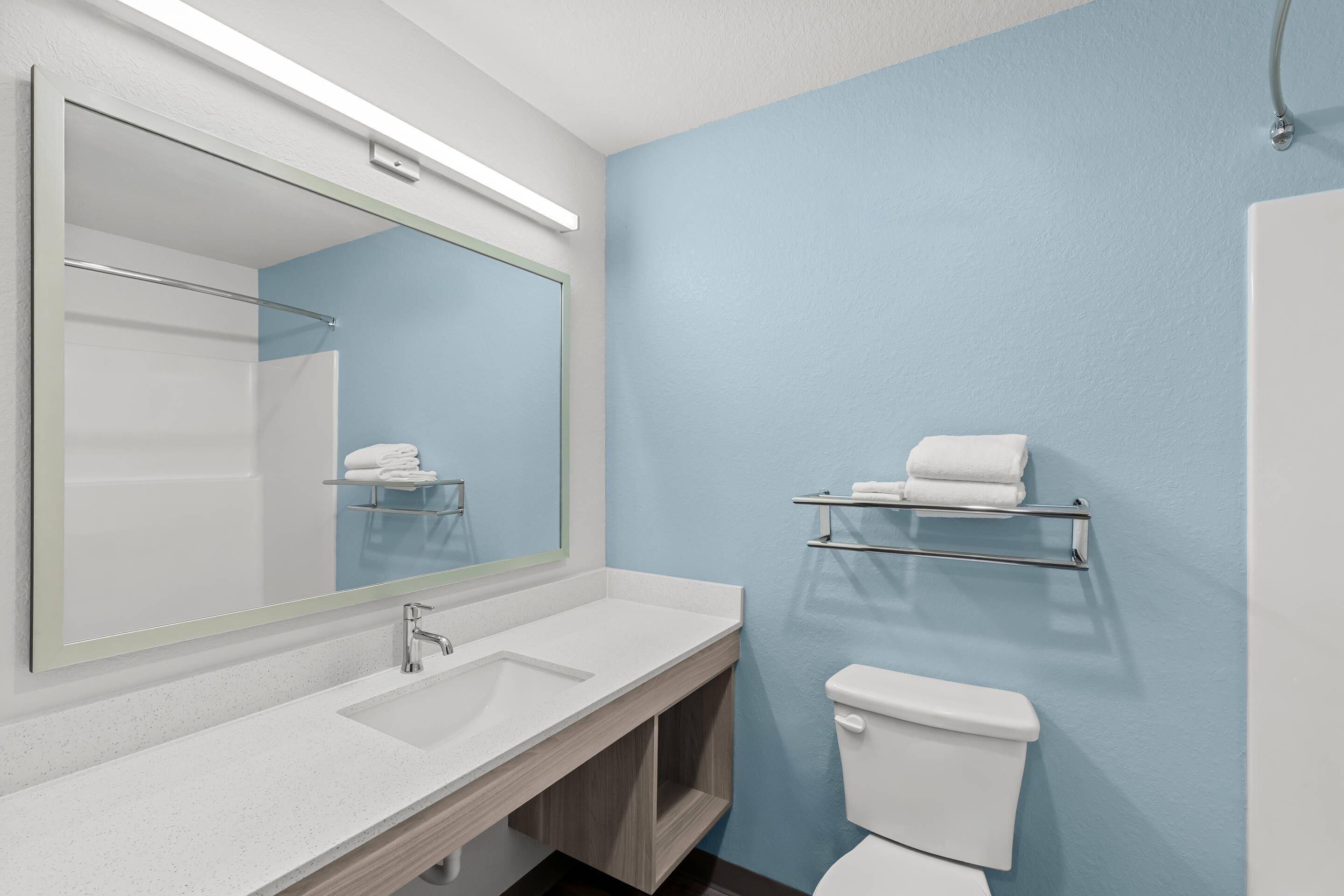 Un baño con un lavamanos blanco, un espejo grande, un inodoro y un perchero para toallas.
