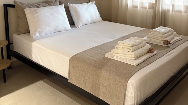 Una habitación de hotel con cama, almohadas, una mesita de noche y una ventana con cortinas.