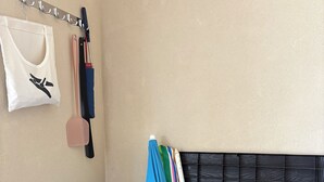 Una habitación con una cama, un gancho en la pared con una bolsa blanca y un baúl con objetos de colores.
