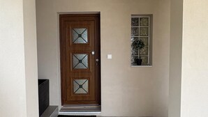 Una puerta con un diseño geométrico de vidrio, una pequeña ventana con una planta y una entrada sencilla con felpudo.