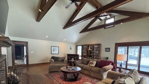 A spacious living room with a high ceiling, wooden beams, a fireplace, a large window, and a cozy seating area with a coffee table. - Large private home in gated horse farm in the heart of horse country! (Lexington)