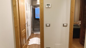 A hallway with wooden doors, a white radiator, a thermostat, and a switch on the wall.