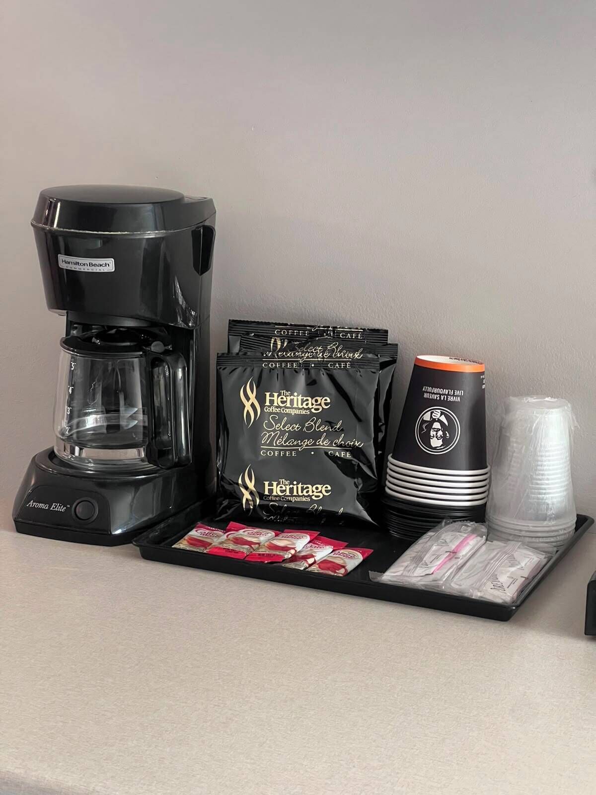 A coffee maker, coffee bags, a coffee cup, and disposable cups on a tray.